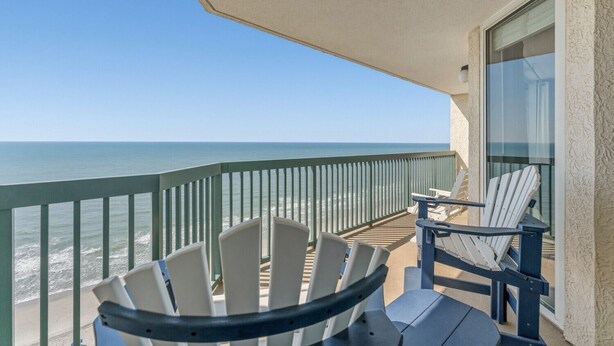 A balcony with a view of the ocean, two Adirondack chairs, and a glass door. - Beachfront Condo, AshWorth, Free Wifi, Pools, Hot Tub | AshWorth - 1806 (North Myrtle Beach)