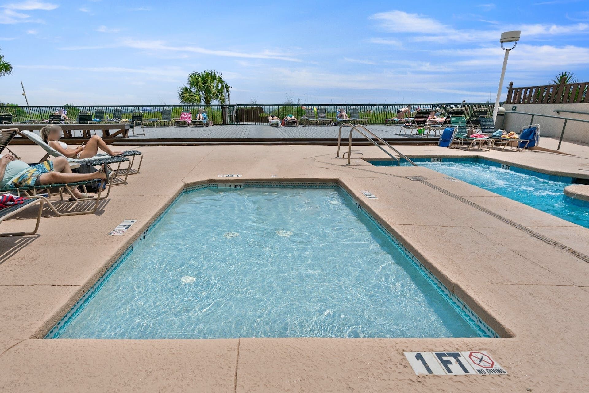 A pool area with multiple lounge chairs and a sign indicating a depth of 1 FT.