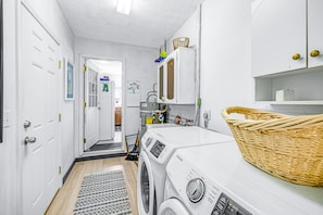 Laundry room with a front-loading washing machine, storage shelf, and broom.