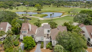 Un campo de golf con un estanque, rodeado de viviendas residenciales con vista al océano.