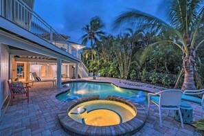 Relax by the pool with a hot tub, lounge chairs, and a patio surrounded by palm trees and tropical vegetation.