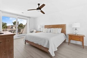 A bedroom with a bed, a nightstand, a ceiling fan, and a view of the outside.