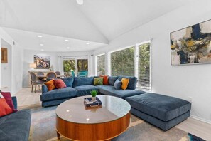 A modern living room with a sectional sofa, a round coffee table, and a dining area in the background.