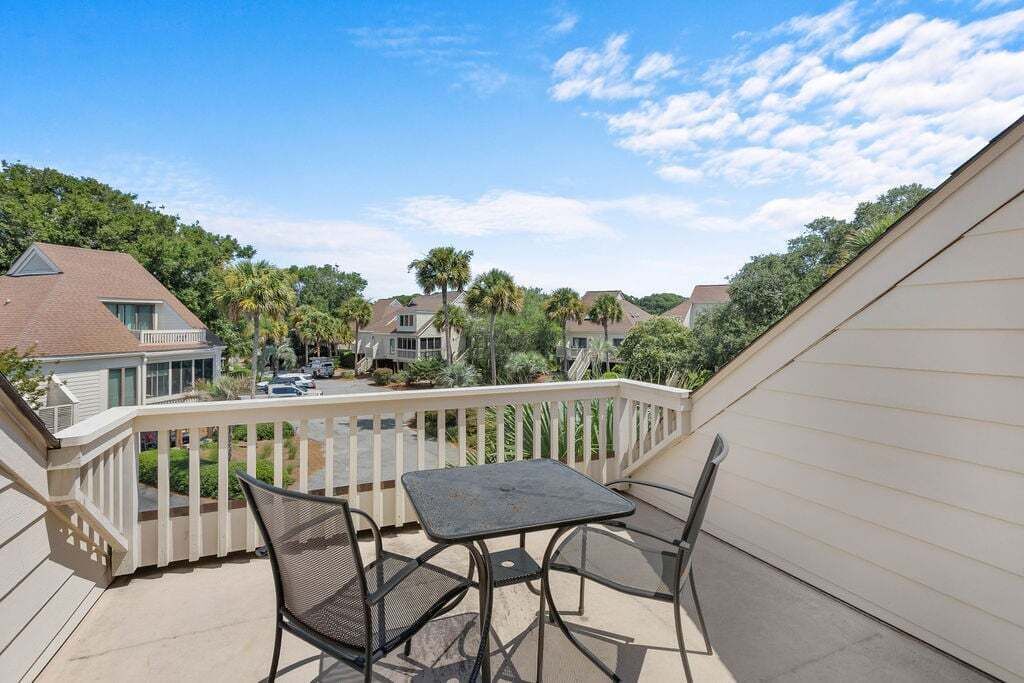 A balcony with a table and chairs, overlooking a residential area with houses and palm trees.
