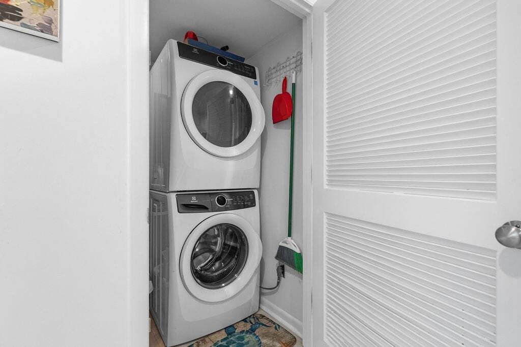 A laundry room with stacked washing machines, a broom, and a mop.