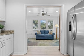 A kitchen with white cabinetry, a stainless steel refrigerator, and a blue sofa with patterned cushions.