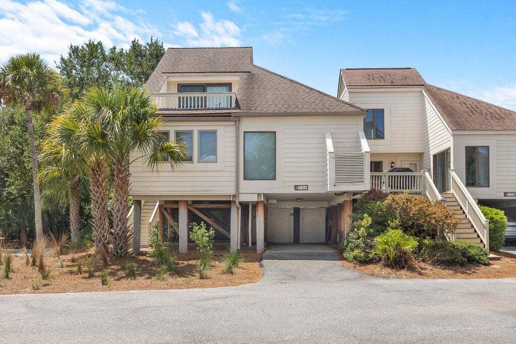 A two-story residential building with a covered garage, a front porch, and a small landscaped area with palm trees.