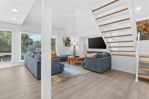 Un salon moderne avec un escalier, des canapés, une table basse et un téléviseur.