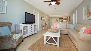 A living room with a television, wicker furniture, a white coffee table, and a ceiling fan. - BEACH FRONT! Waterscape A411 SLEEPS 8 OCEAN FRONT! LAZY RIVER! (Fort Walton Beach)