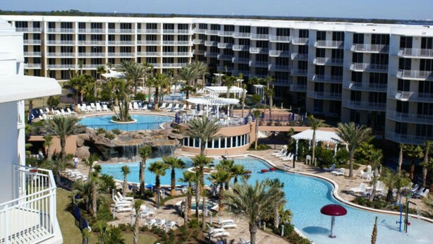 A hotel with multiple balconies, a central pool area with palm trees, and a separate pool with a waterfall feature. - BEACH FRONT! Waterscape A411 SLEEPS 8 OCEAN FRONT! LAZY RIVER! (Fort Walton Beach)