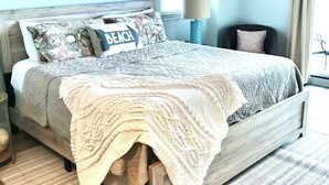 A bedroom with a wooden bed, a ceiling fan, a window with blinds, a lamp, and a wall-mounted paddleboard. - BEACH FRONT! Waterscape A411 SLEEPS 8 OCEAN FRONT! LAZY RIVER! (Fort Walton Beach)