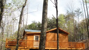 A wooden cabin with a balcony, surrounded by trees.