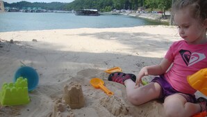 Un bambino gioca con dei castelli di sabbia su una spiaggia, con delle barche sullo sfondo.