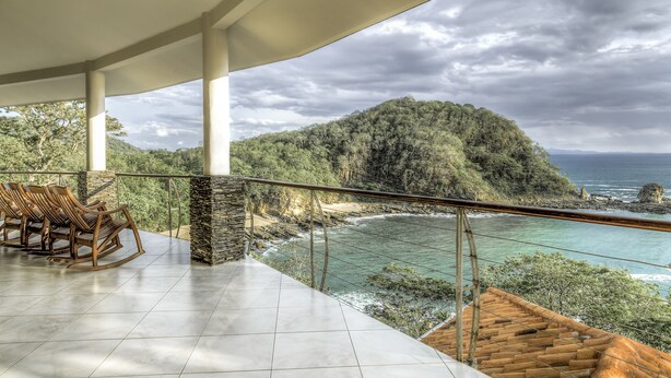 Un balcón con vistas a un paisaje costero, que incluye una playa y una colina arbolada.