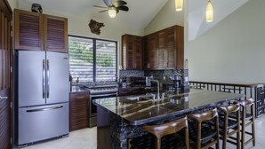 Una cocina moderna con una isla central, electrodomésticos de acero inoxidable, armarios de madera e iluminación colgante.