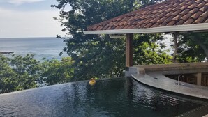 Una piscina con vista al mar, rodeada de árboles y un edificio con techo de tejas.