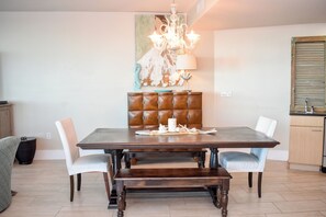 A dining area with a wooden table, cushioned chairs, a bench, a chandelier, and a painting on the wall. - 9th Flr Luxury 4BR Condo- Panoramic Waterfront Views - Rooftop Pool & Lazy River (Orange Beach)