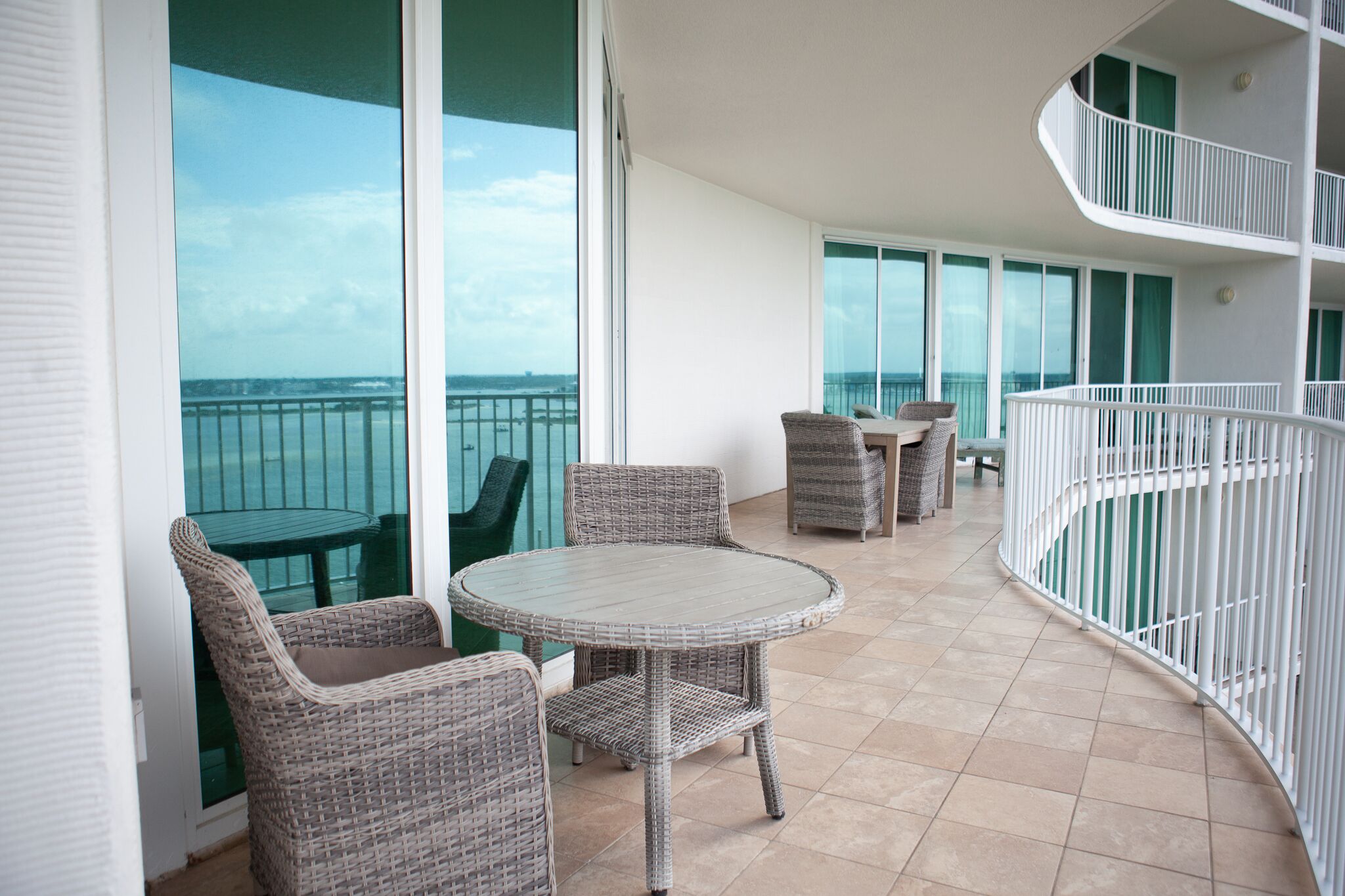 Un balcón con mobiliario de mimbre, una mesa de vidrio y vistas al mar.