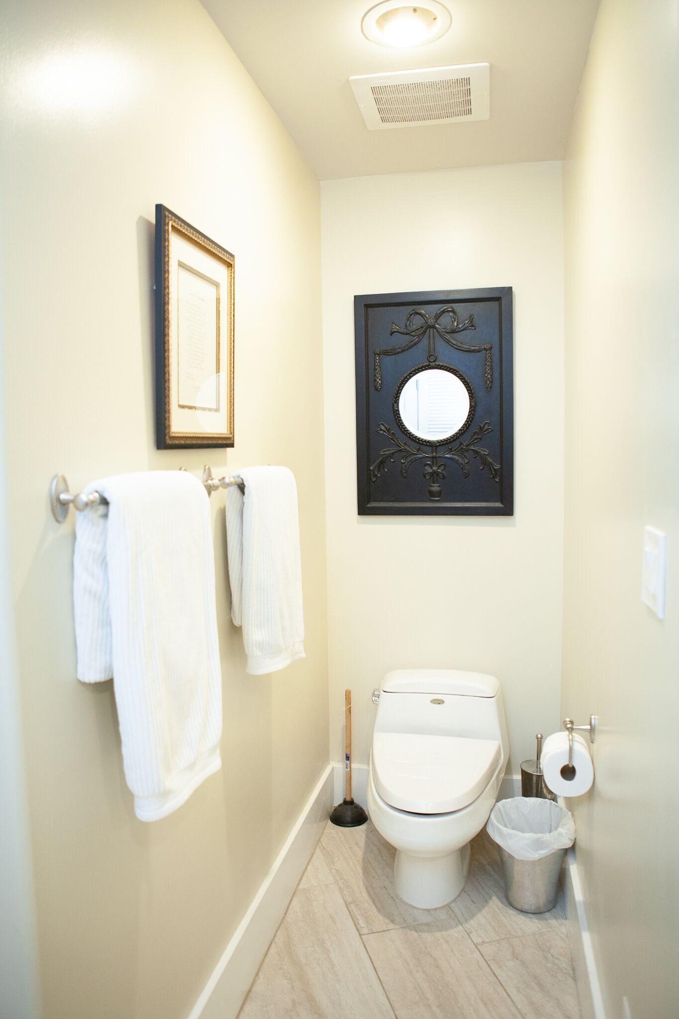Een badkamer met twee handdoeken aan een handdoekrek, een toilet, een bidet, een prullenbak en twee ingelijste foto’s aan de muur.