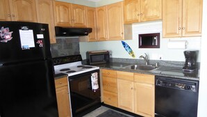 A kitchen with wooden cabinets, a black refrigerator, a stove, a microwave, and a dishwasher. - FULL OCEAN VIEW, 2nd Floor 2 BR/1 BA,  BEST STAND-UP PADDLEBOARDING ON MAUI! (Kihei)