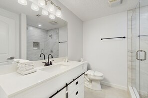 Bathroom features a large mirror above a vanity with sink, toilet, and glass shower enclosure.