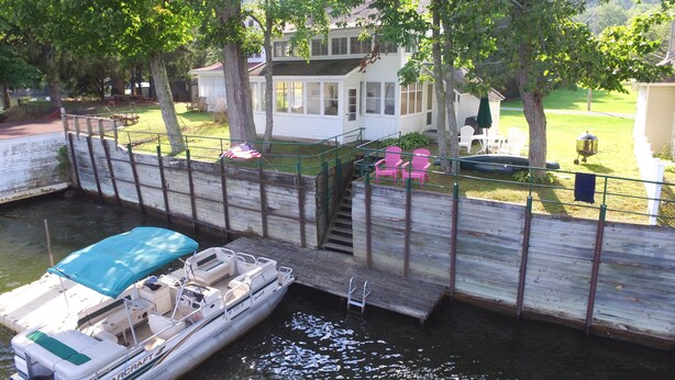 A dock with a boat, a wooden pier, and a house with a deck and outdoor seating.