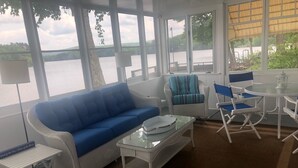 A room with a blue sofa, wicker chairs, a glass table, and a view of a lake.