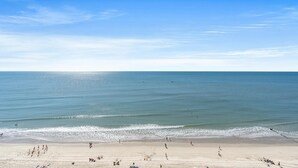 A beach with a clear sky, calm sea, and people walking along the shore. - Spacious Condo, Whirlpool Tub, Oceanfront Lazy River | Crescent Shores - S 1306 (North Myrtle Beach)
