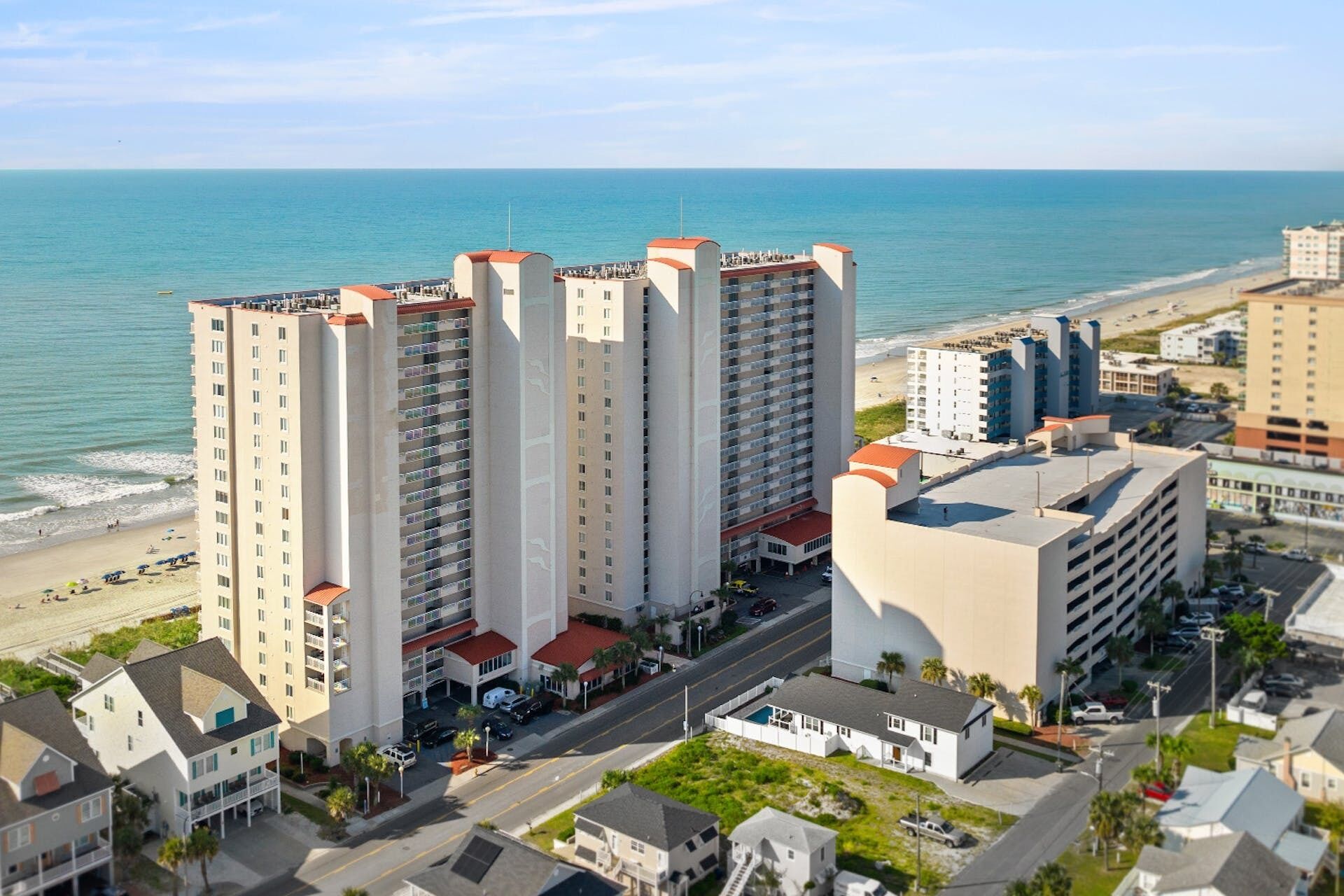 A high-rise hotel with multiple balconies, located near a beach with a clear view of the ocean.