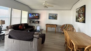 A spacious living area with a sofa, a wooden dining table with chairs, a foosball table, and a ceiling fan.