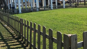 A blue building with a balcony, a wooden fence, and a grassy area.