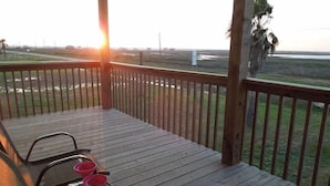 A wooden deck with a railing, a table with chairs, and a view of the beach and ocean.