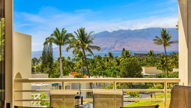 Un balcón con vistas a palmeras, montañas y una masa de agua.