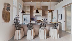 A kitchen with wooden cabinets, a central island with bar stools, hanging pendant lights, and a rustic wooden ceiling. - Elegant interior. Sunset views. Walk to town. Professional kitchen. Pet friendly (Highlands)