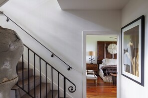 A staircase with a stone accent, a wooden floor, a bed with white bedding, a lamp, and a framed artwork on the wall.