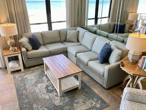 Una sala moderna con un amplio sofá modular, una mesa de centro de madera y vista a la playa.