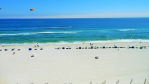 Une plage avec un ciel dégagé, un rivage sablonneux, quelques parasols et des chaises de plage.