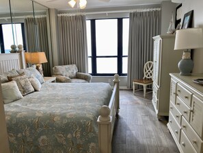 Une chambre à coucher avec un lit, une chaise, une commode et une grande fenêtre.
