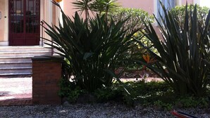 A building with a red door, a balcony, and a garden with palm trees and other plants. - Blue Riviera: a splendid beachfront 1-bedroom apt w/stunning view (Menton)