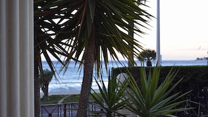 A view of the ocean through a window, with palm trees and a railing in the foreground. - Blue Riviera: a splendid beachfront 1-bedroom apt w/stunning view (Menton)