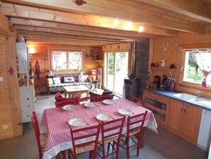 A wooden cabin interior with a dining area, kitchen, and a fireplace. - Chalet Érable**** - Sauna - 8 Pers | Household, Towels & Beds Made Included (Rochesson)