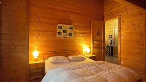 A wooden cabin bedroom with a large bed, two bedside lamps, and a framed picture on the wall. - Chalet Érable**** - Sauna - 8 Pers | Household, Towels & Beds Made Included (Rochesson)