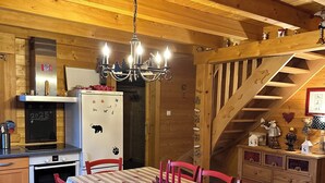 A cozy wooden cabin interior with a dining table, chairs, a kitchen area, and a staircase. - Chalet Érable**** - Sauna - 8 Pers | Household, Towels & Beds Made Included (Rochesson)