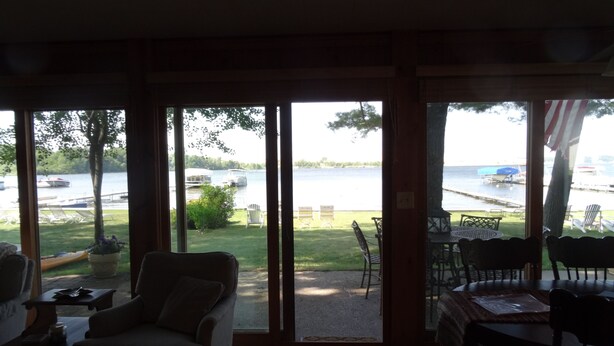 Une pièce dotée d’une grande porte-fenêtre coulissante donnant sur une terrasse aménagée avec du mobilier d’extérieur et offrant une vue sur un lac où naviguent des bateaux.