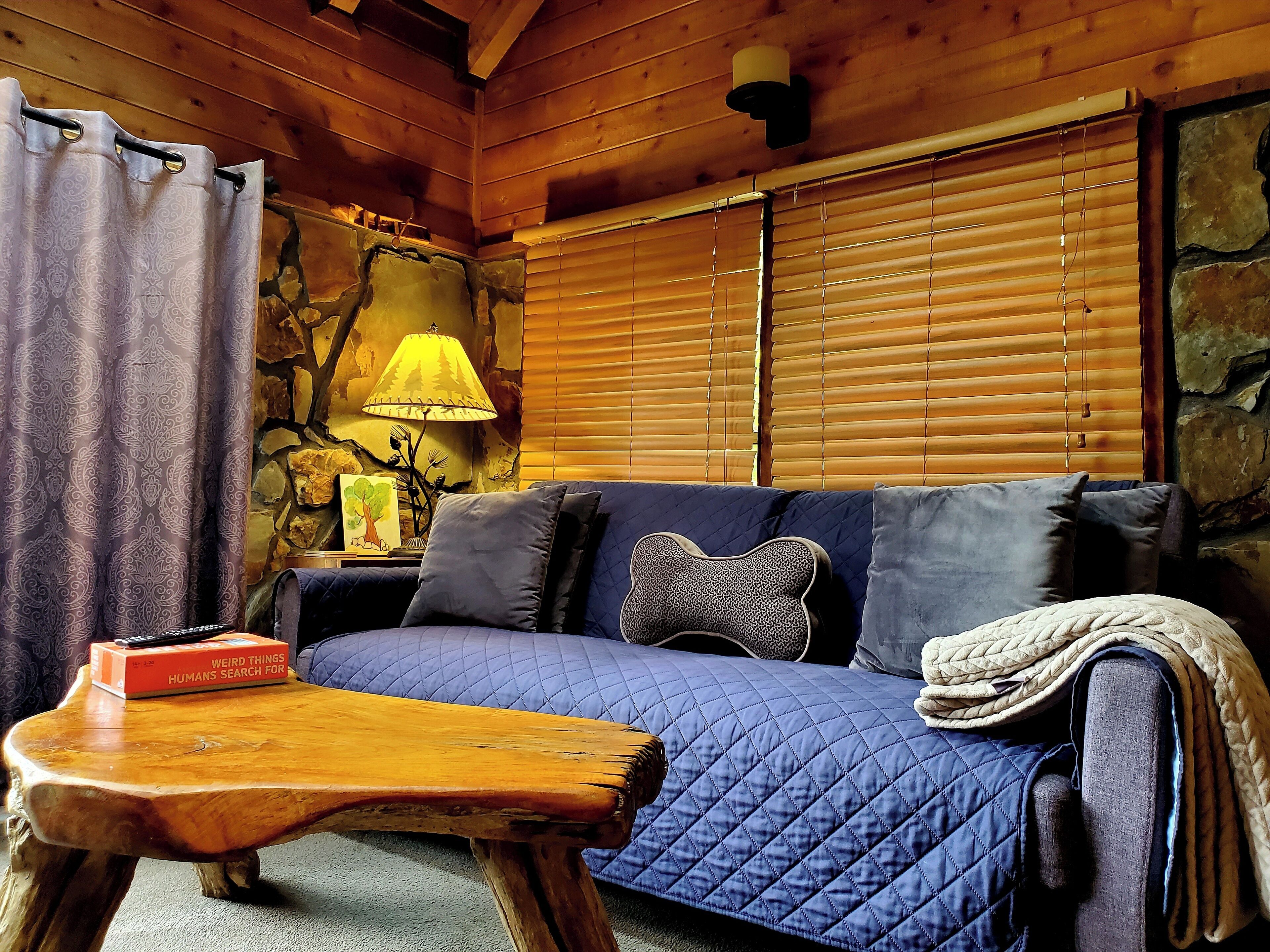 A cozy room with a blue quilted sofa, a wooden coffee table, a lamp, and a stone wall.