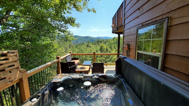Un bain à remous sur une terrasse en bois, avec vue sur une forêt et des montagnes.