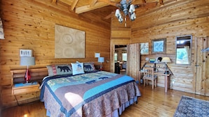 Une chambre située dans un chalet en rondins, avec un grand lit, des murs en bois, un ventilateur de plafond et un bureau avec une chaise.