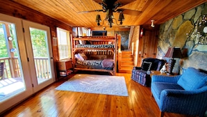 L’intérieur chaleureux d’un chalet avec un plancher en bois, un lit superposé, un fauteuil bleu et un mur en pierre.