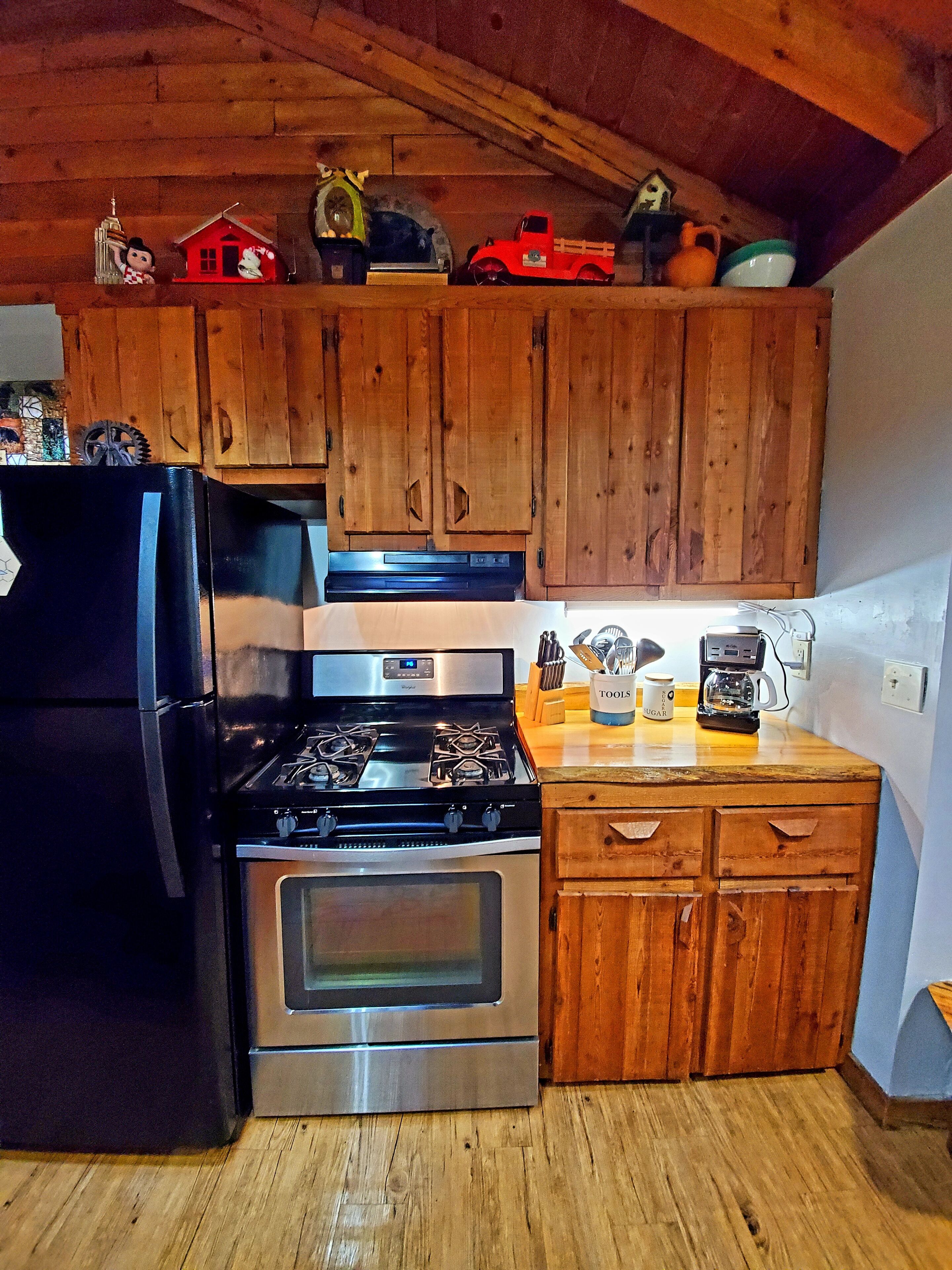 Une cuisine avec des meubles de rangement en bois, un réfrigérateur noir, une cuisinière en acier inoxydable et une machine à café posée sur le plan de travail.