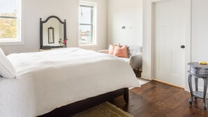 Een slaapkamer met een bed, een stoel, een klein tafeltje, een spiegel en een deur.